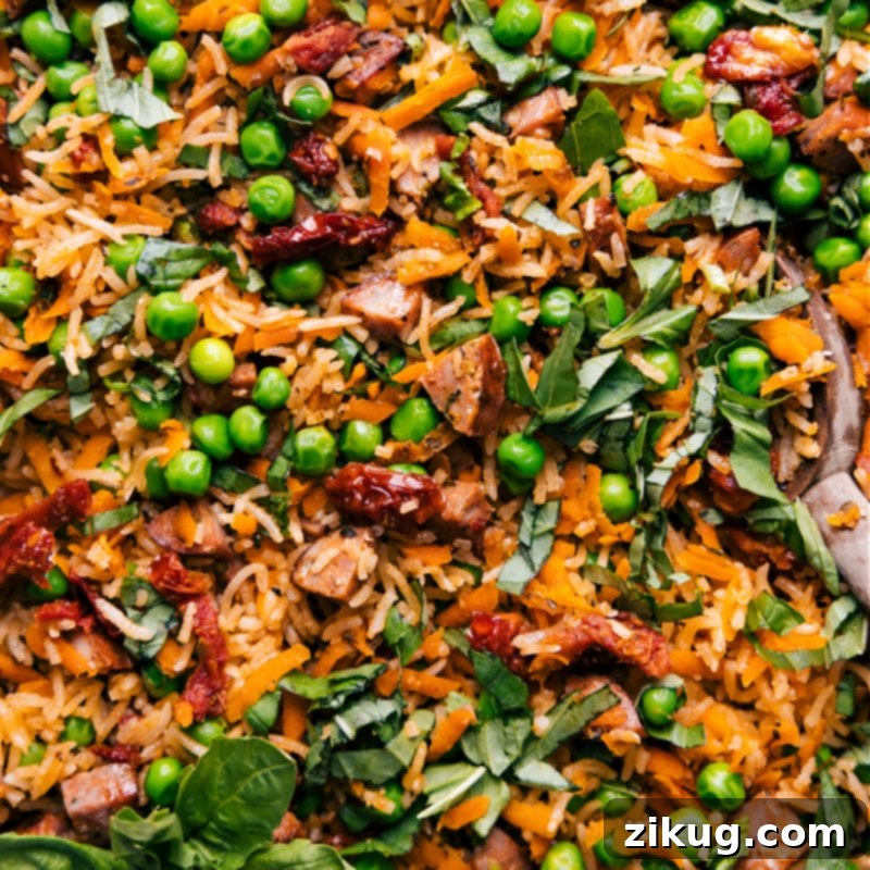 A close-up view of the perfectly cooked One-Pan Pesto Rice, showcasing its tender grains, bits of smoked chicken sausage, and colorful vegetables, all coated in a light green pesto sauce.