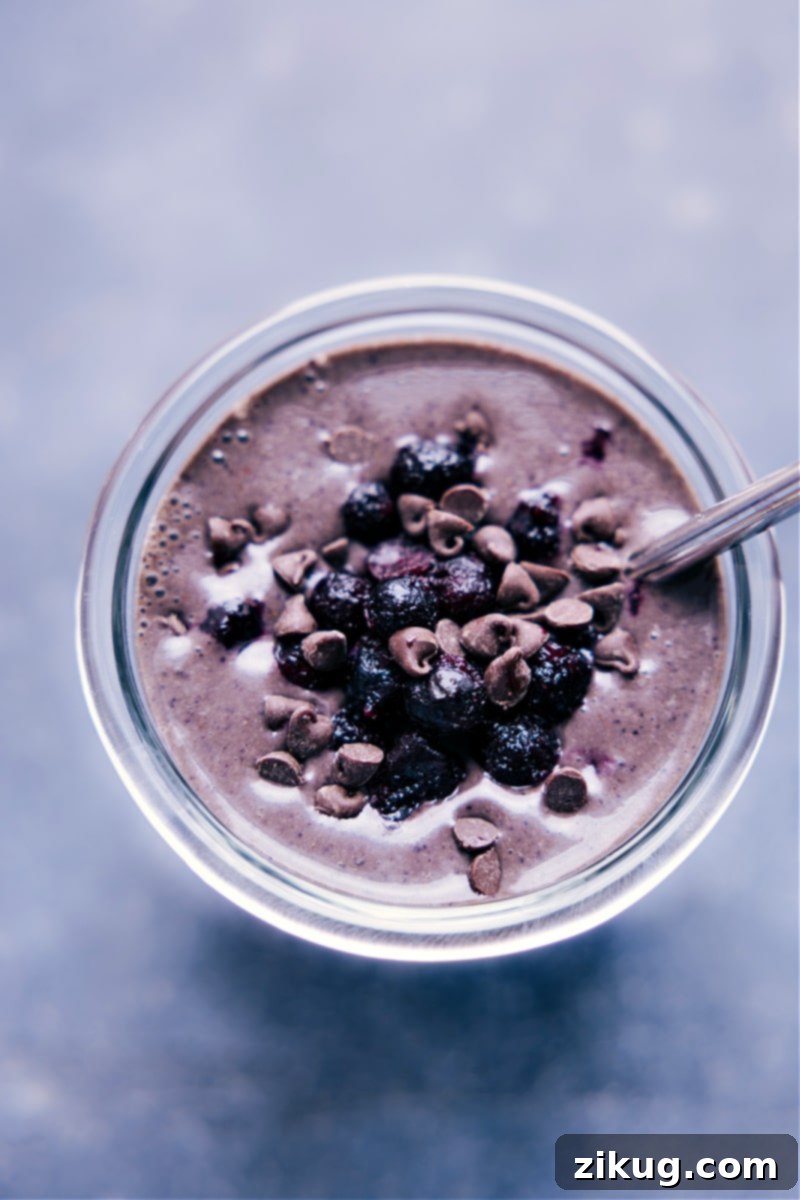 Homemade Chocolate Blueberry Smoothie: A nutritional powerhouse for breakfast or snack, inspired by Daily Harvest. Recipe via ChelseasMessyApron.com #smoothie #chocolateblueberry #chocolate #blueberry #breakfast #protein #healthy #filling Overhead view of a rich, dark Chocolate Blueberry Smoothie in a glass, garnished with fresh blueberries and chocolate shavings.