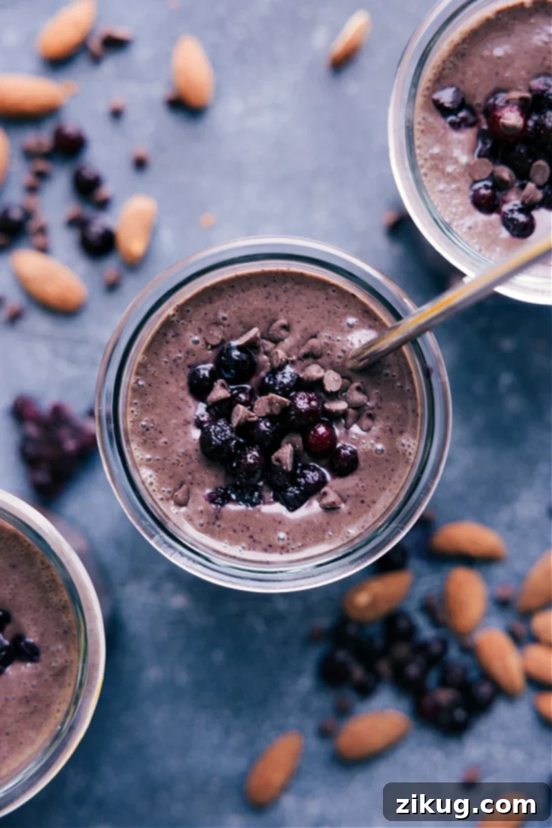 Delicious & Refreshing Chocolate Blueberry Smoothie - A perfect healthy start to your day or a nourishing snack! Recipe via ChelseasMessyApron.com #smoothie #chocolateblueberry #chocolate #blueberry #breakfast #protein #healthy #filling A top-down view of a vibrant Chocolate Blueberry Smoothie in a clear glass, garnished with a few fresh blueberries, sitting on a light wooden surface.