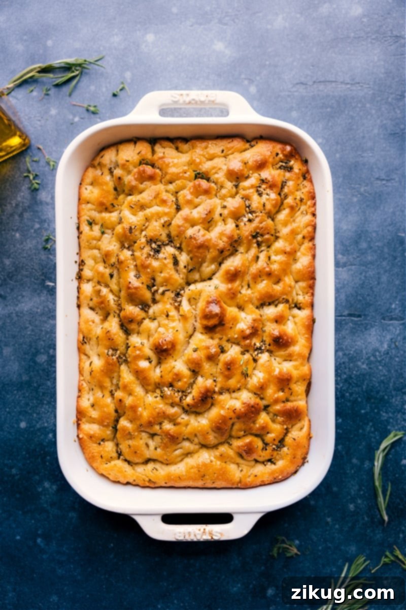 Beautifully baked herbed focaccia, fresh from the oven, garnished with vibrant rosemary and sparkling flaky sea salt, ready to be served.
