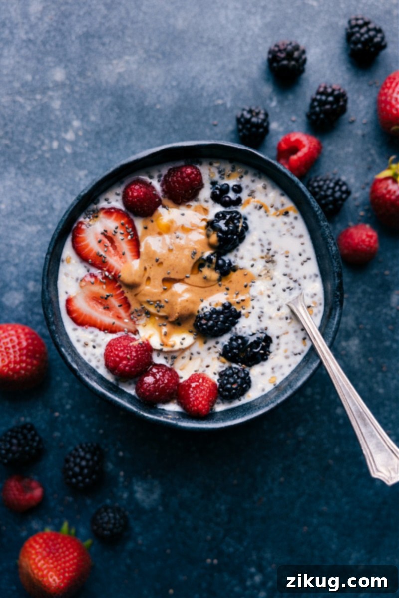 The easiest ever Overnight Oats With Chia Seeds -- only three ingredients and a couple minutes of prep time for a filling and nutritious breakfast! Recipe via ChelseasMessyApron.com #overnightoats #oats #healthy #breakfast #quick #yummy #chiaseeds #chia #vegetarian Overhead view of creamy Overnight Oats with Chia Seeds, artfully topped with fresh berries, sliced almonds, and a drizzle of rich nut butter, ready to be enjoyed as a healthy and quick breakfast.