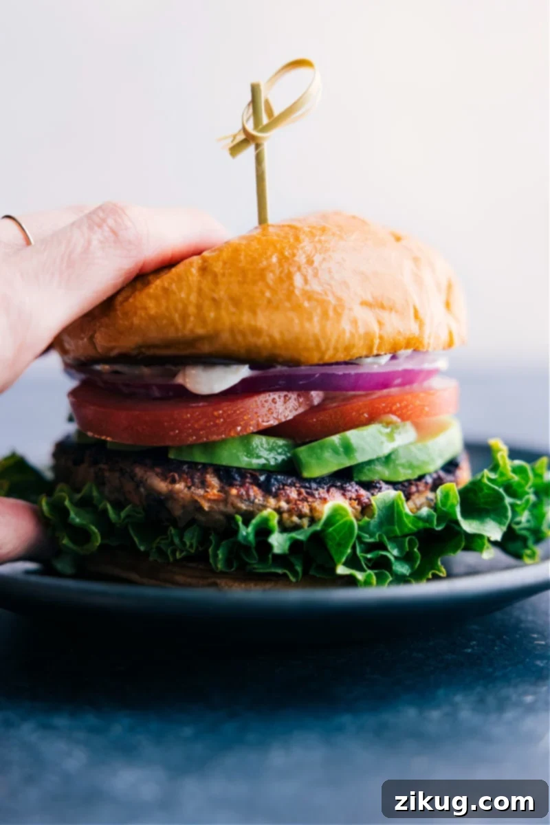 A perfectly stacked Veggie Burger, featuring a thick patty, crisp lettuce, creamy avocado, ripe tomatoes, thinly sliced onions, and a generous dollop of special sauce, all nestled in a soft brioche bun.