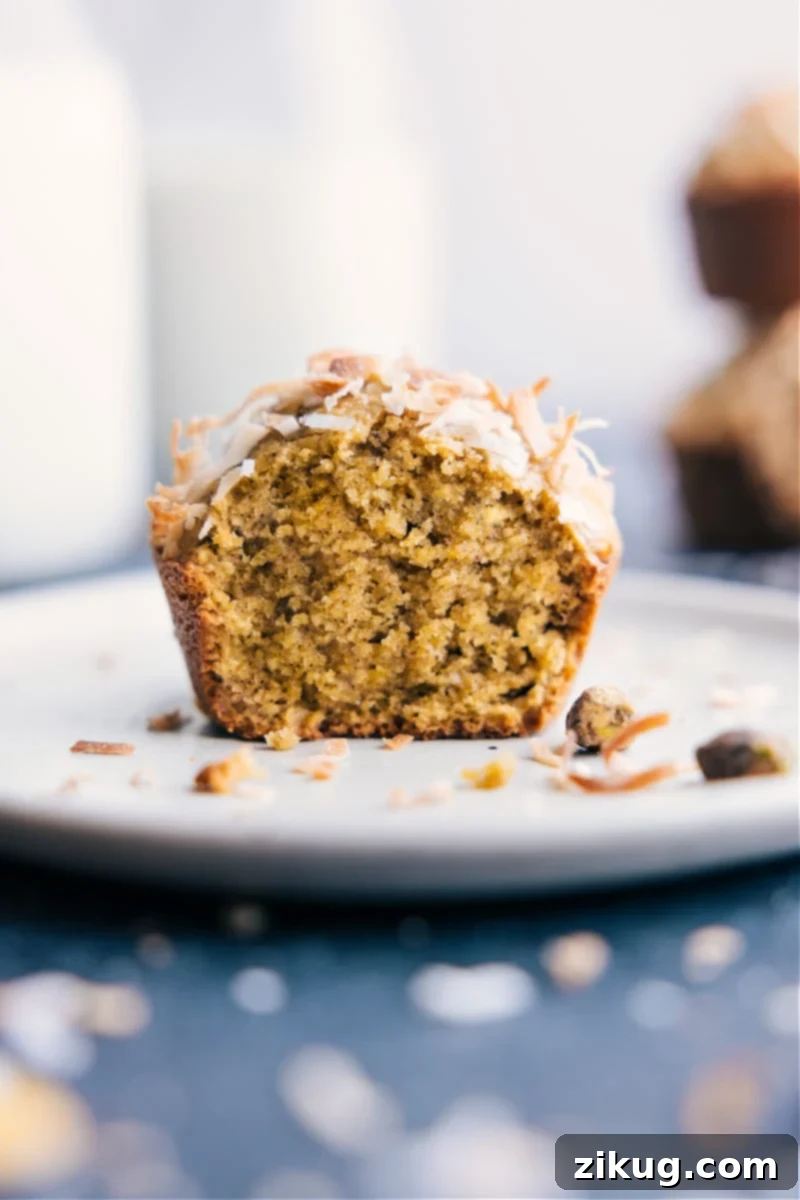 Enjoying a bite of a freshly baked Pistachio Muffin: a quick, easy, and undeniably delicious treat. A single Pistachio Muffin on a plate with a bite taken out, revealing its moist, green-flecked interior.