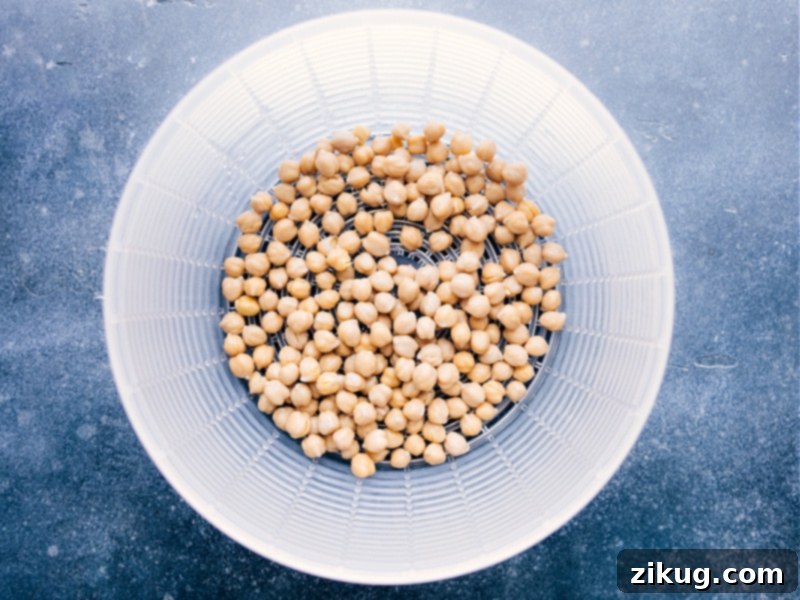 Preparing Buffalo Chickpea Salad: Draining and rinsing chickpeas for optimal texture and flavor. Quick and easy vegetarian recipe. An overhead shot illustrating the crucial step of thoroughly draining and rinsing chickpeas in a colander, essential for achieving the optimal texture and flavor in Buffalo Chickpea Salad.
