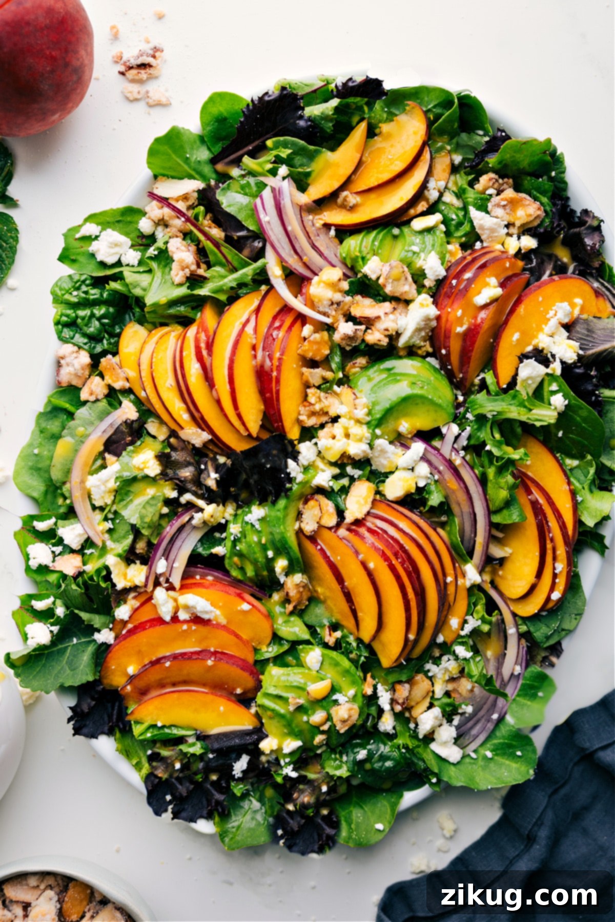 Fresh And Flavorful Peach Salad Recipe A vibrant peach salad featuring fresh peaches, thinly sliced red onions, crumbled feta cheese, and homemade candied almonds, all served over a bed of crisp lettuce and drizzled with a tangy citrus dressing.