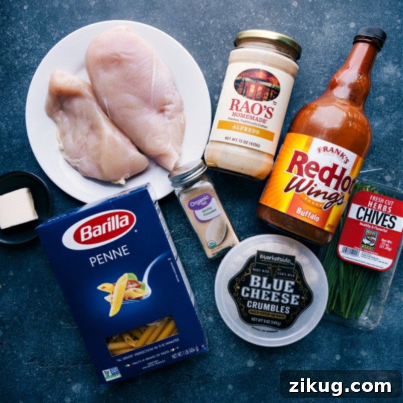 Collection of fresh ingredients for Buffalo Chicken Pasta including raw chicken breasts, penne pasta, Alfredo sauce, buffalo sauce, butter, peas, and seasonings.