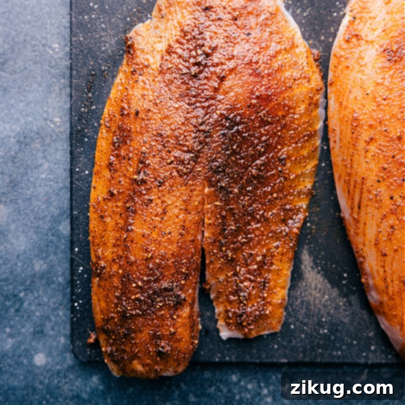 Seasoned tilapia fillets prepped for air frying, ensuring a quick, healthy, and flavorful meal. Overhead view of several raw tilapia fillets generously coated with a vibrant spice rub, neatly arranged on a tray, ready to be cooked in the air fryer.