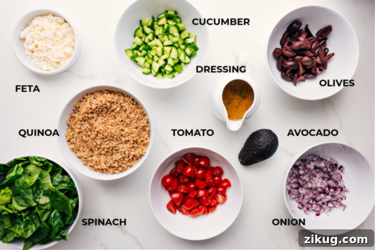 Fresh ingredients for Greek Quinoa Salad, including cooked quinoa, spinach, cherry tomatoes, Kalamata olives, cucumber, red onion, avocado, and feta cheese, neatly arranged on a counter.