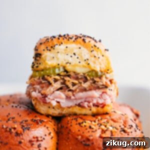 Close-up of a stack of golden Cuban Sliders, revealing layers of pork, ham, Swiss cheese, and pickles.