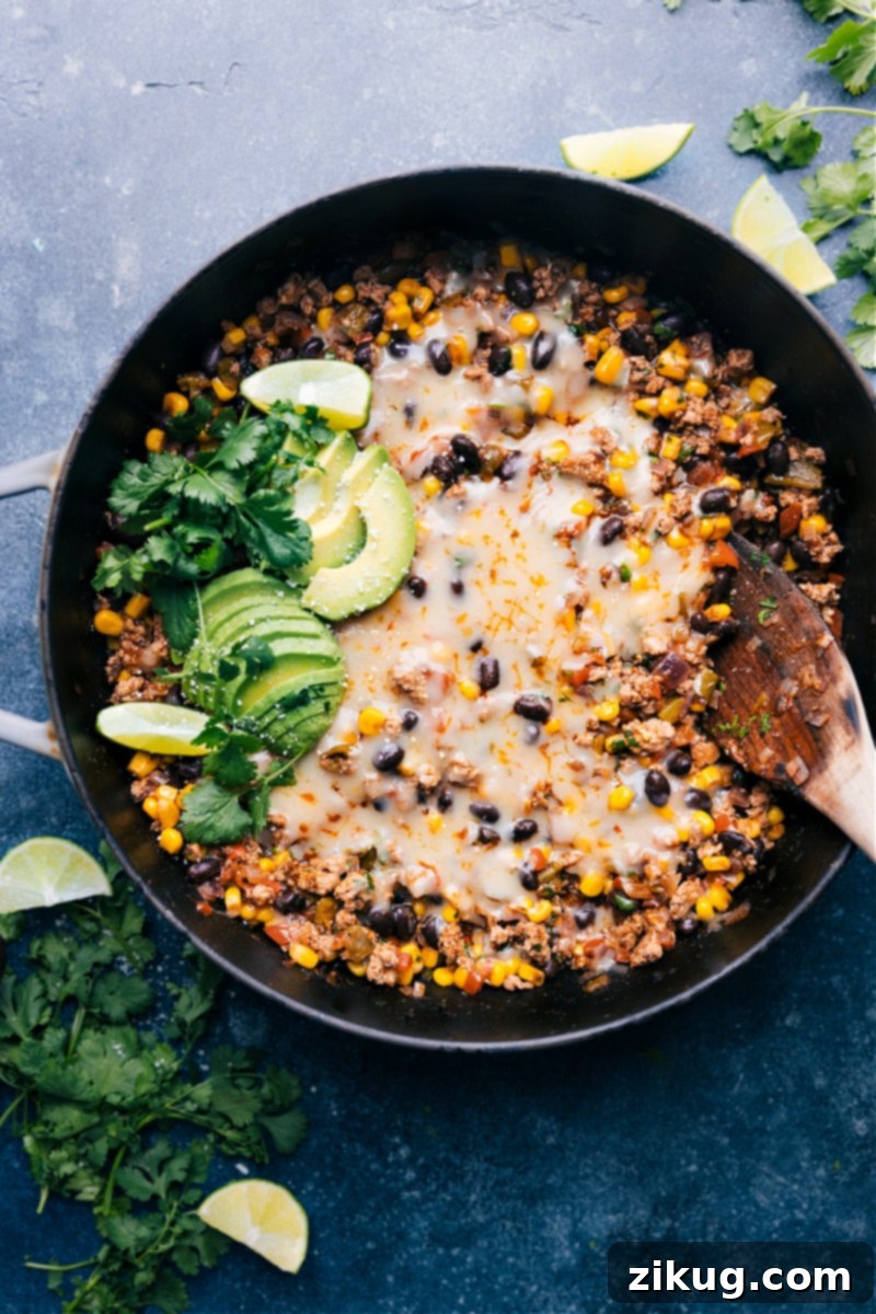 This savory Green Chile Ground Turkey skillet is an explosion of flavor, featuring perfectly seasoned ground turkey, black beans, crisp corn, and a saucy fire-roasted green chiles base. An easy, 30-minute weeknight dinner! Recipe via ChelseasMessyApron #dinner #quick #easy #simple #best #fresh #healthy #wholefoods #cleaneating #familyfriendly #kidfriendly #greenchile #groundturkey Up-close, inviting overhead image of the Green Chile Ground Turkey, showcasing the melted cheese, vibrant ingredients, and a sprinkle of fresh cilantro.