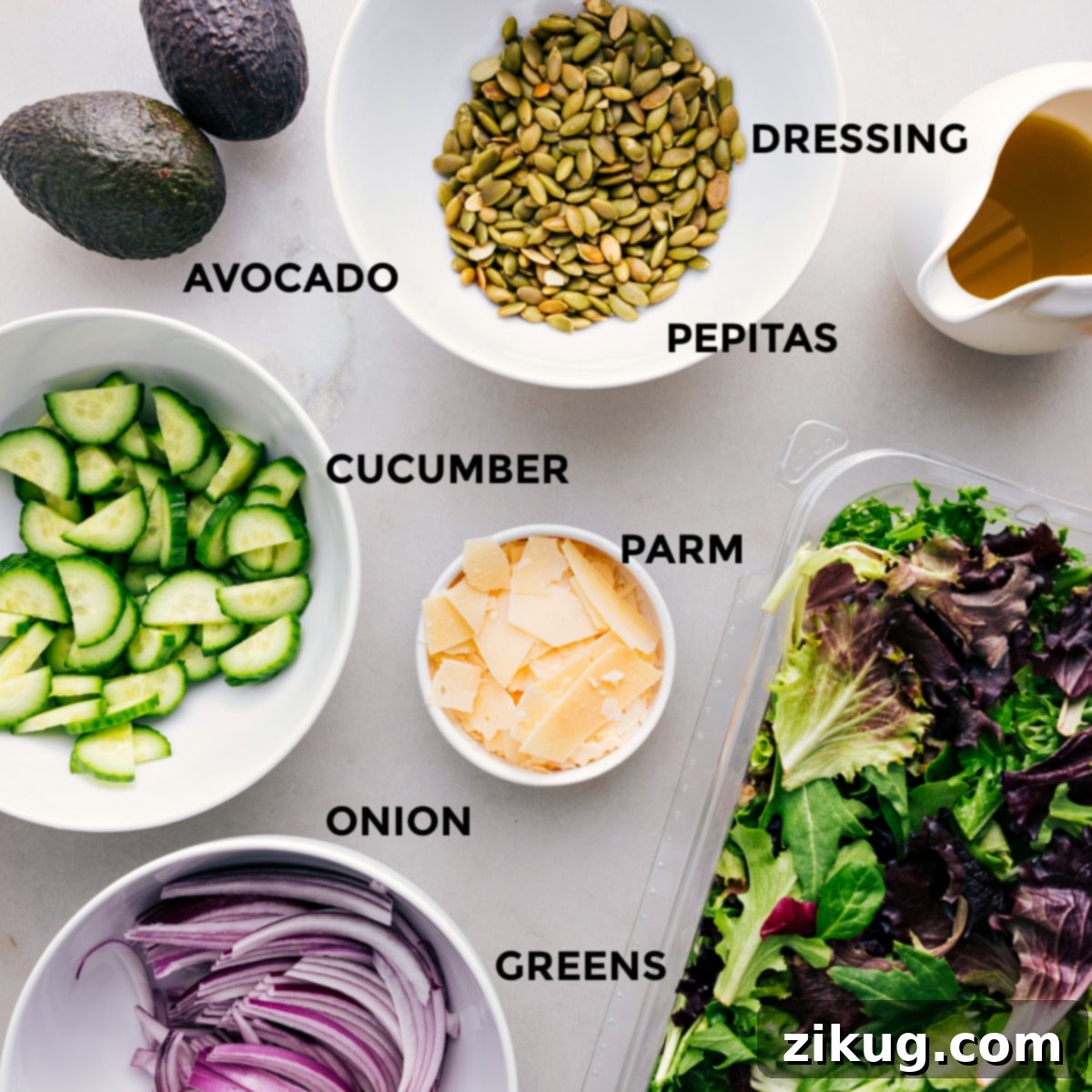 All the ingredients for this recipe—dressing, pepitas, avocado, cucumber, parm, greens, and onion—prepped and ready for easy assembly. A colorful display of fresh salad components.