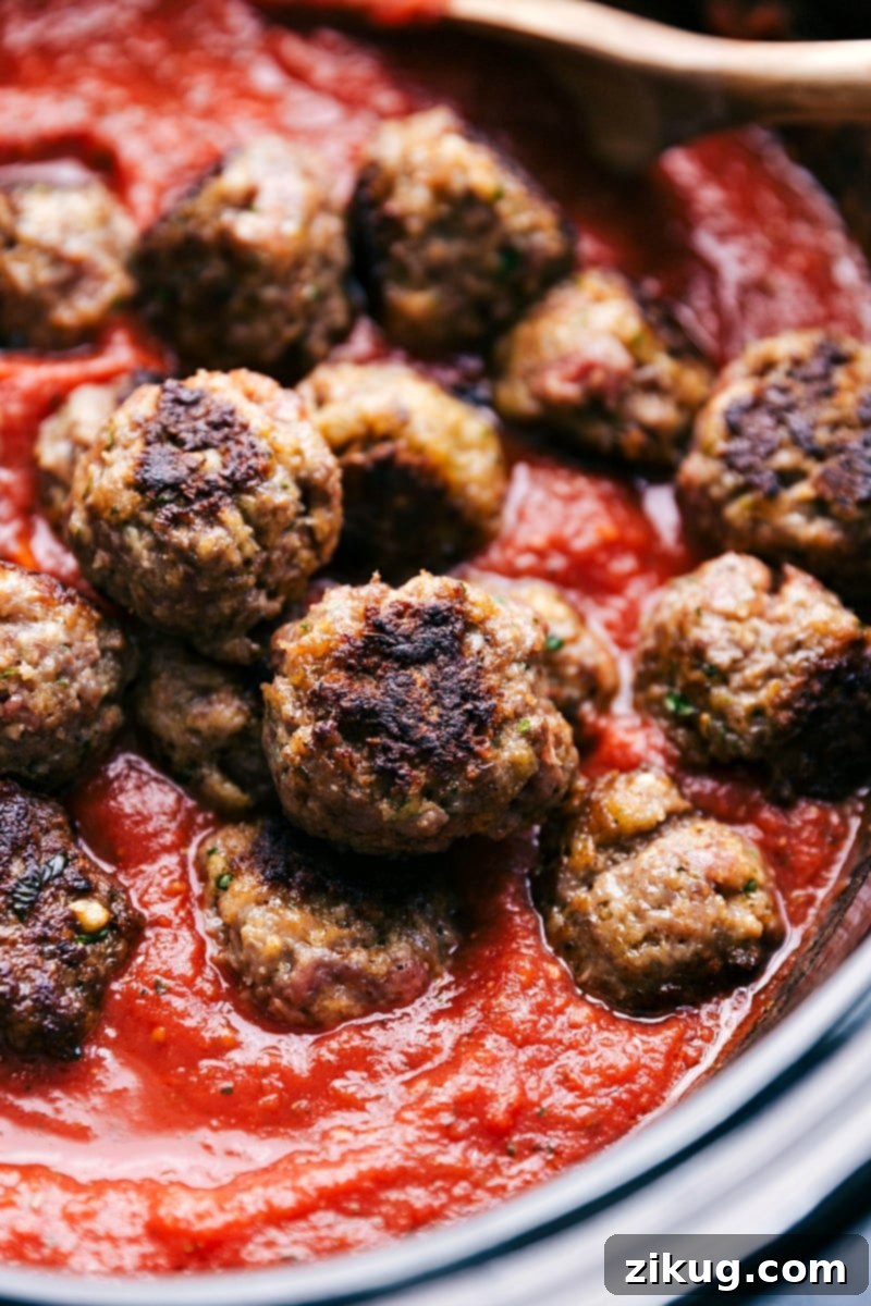 Tender and flavorful meatball sliders with an incredible homemade marinara sauce made in the slow cooker. Add the meatballs and sauce to a slider roll, add cheese, and broil them to make the ultimate meatball sliders. Recipe via chelseasmessyapron #hawaiianrolls #easy #recipes #foracrowd # mini #videos #crockpot #meatball #sliders Up close image of the meatballs being put in marinara sauce for this meatball sliders recipe