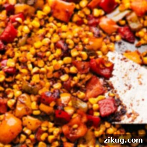 The roasted corn and peppers mixture on a sheet pan, fresh out of the oven with golden-brown kernels.