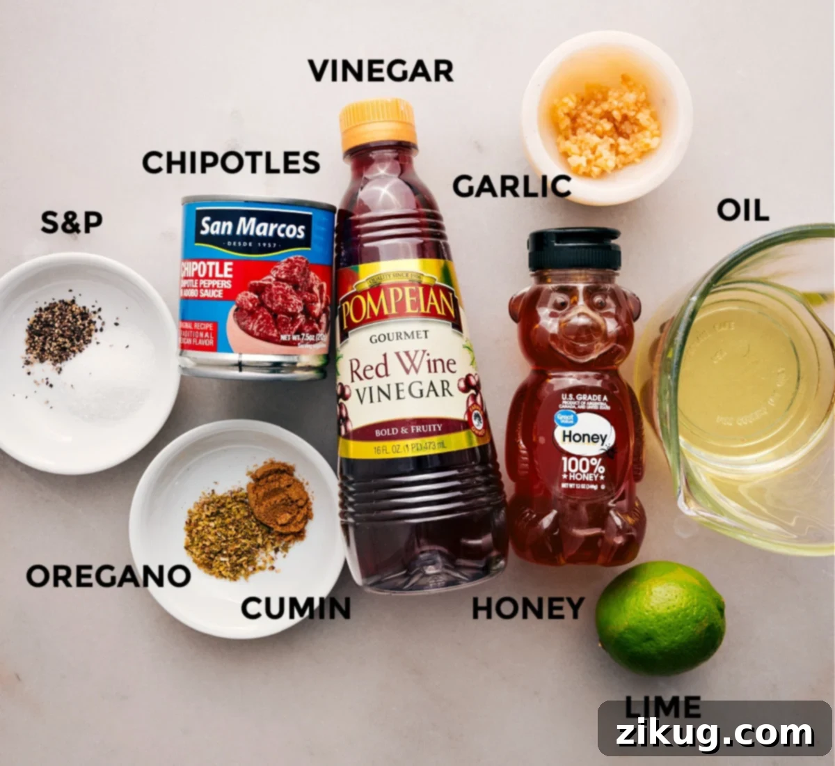 A curated display of all the essential ingredients for making Chipotle Vinaigrette, including fresh lime, honey, red wine vinegar, olive oil, garlic, cumin, oregano, salt, pepper, and a can of chipotles in adobo sauce.