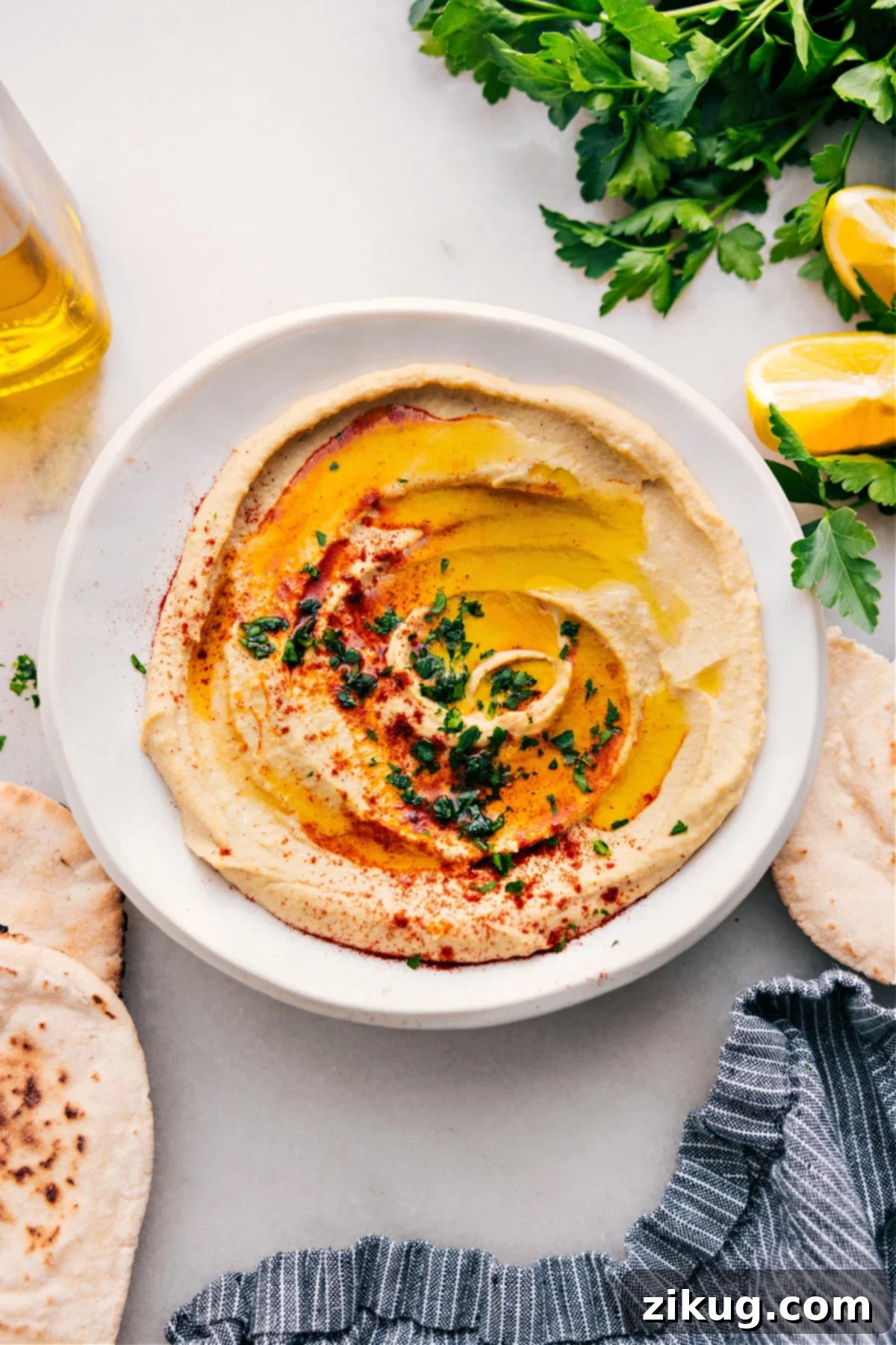 A beautifully presented bowl of creamy homemade hummus, drizzled with fresh olive oil, sprinkled with vibrant paprika, and garnished with delicate herbs.