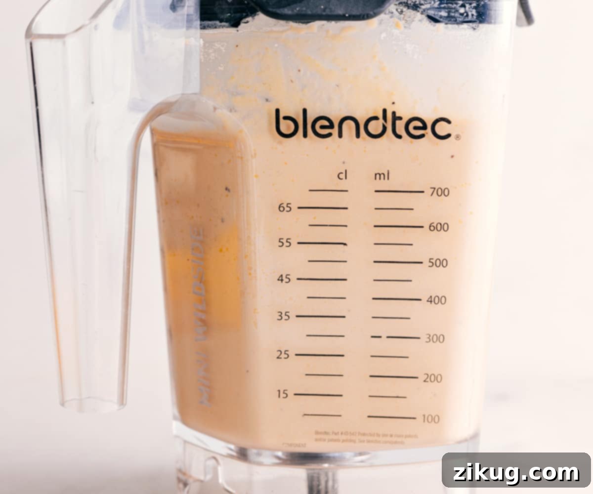 The hummus mixture inside the blender has achieved a perfectly smooth and creamy consistency, indicating a successful blend and readiness for serving.
