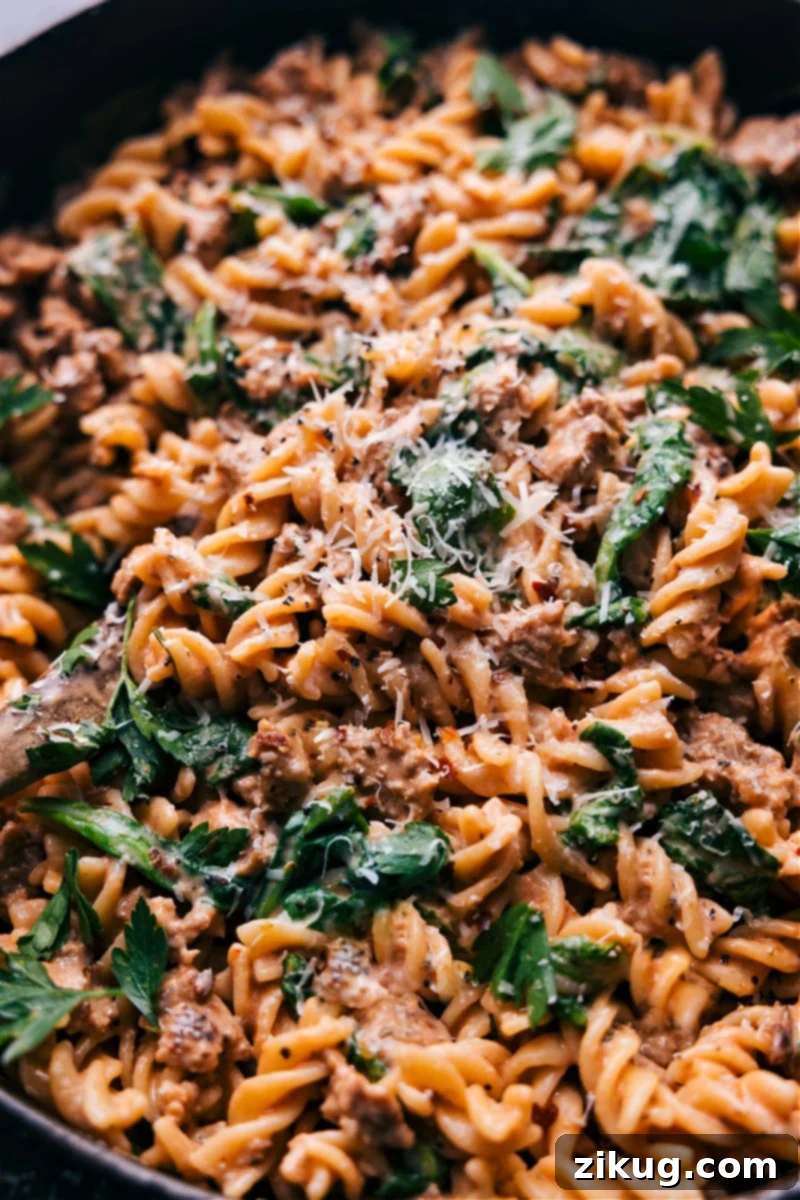 Sausage Pasta: Italian sausage in a creamy tomato sauce with fresh baby spinach and tender pasta, topped with Parmesan. A quick, easy, and family-friendly comfort food dinner. #dinner #quick #easy #simple #best #familyfriendly #kidfriendly #comfortfood #cheesy #sausage #pasta Overhead image of a delectable sausage pasta dish, ready to be served, garnished with fresh herbs.