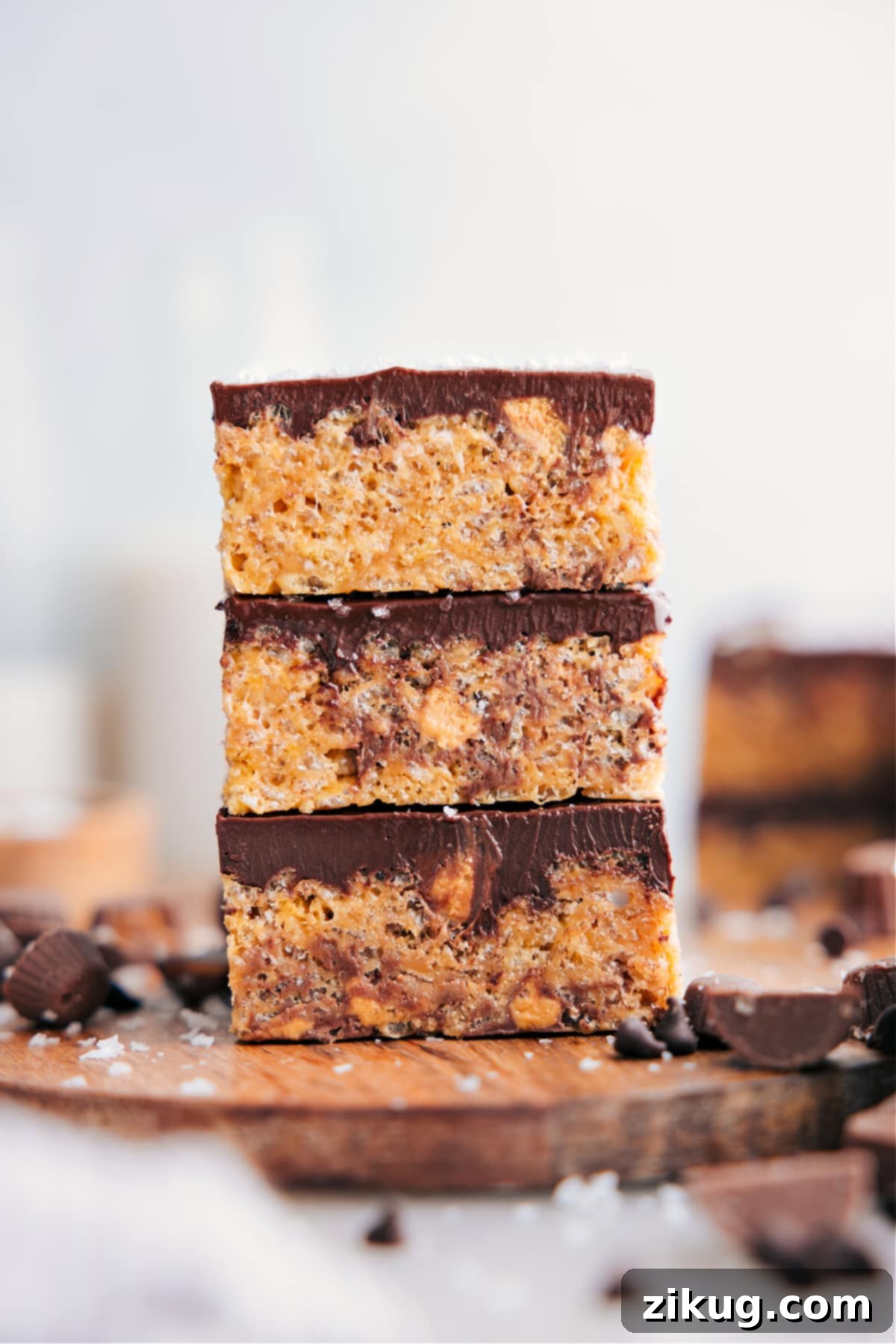 The Best Peanut Butter Rice Krispie Treats Recipe Peanut Butter Rice Krispie Treats cut into squares and stacked on top of each other, showcasing the chocolate topping and peanut butter cups inside.