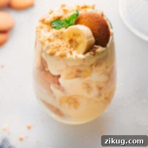 A stunning close-up of a glass brimming with layers of homemade banana pudding, featuring creamy custard, tender vanilla wafers, and fresh banana slices, crowned with a sprinkle of crushed cookies.