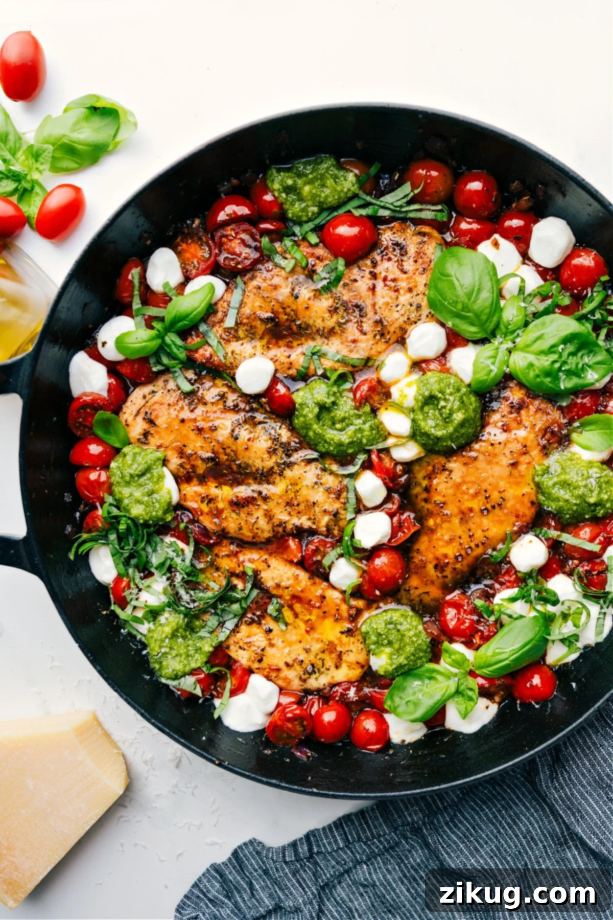 Skillet Caprese chicken with fresh pesto, melted mozzarella, and tomatoes cooked together, ready to be served.