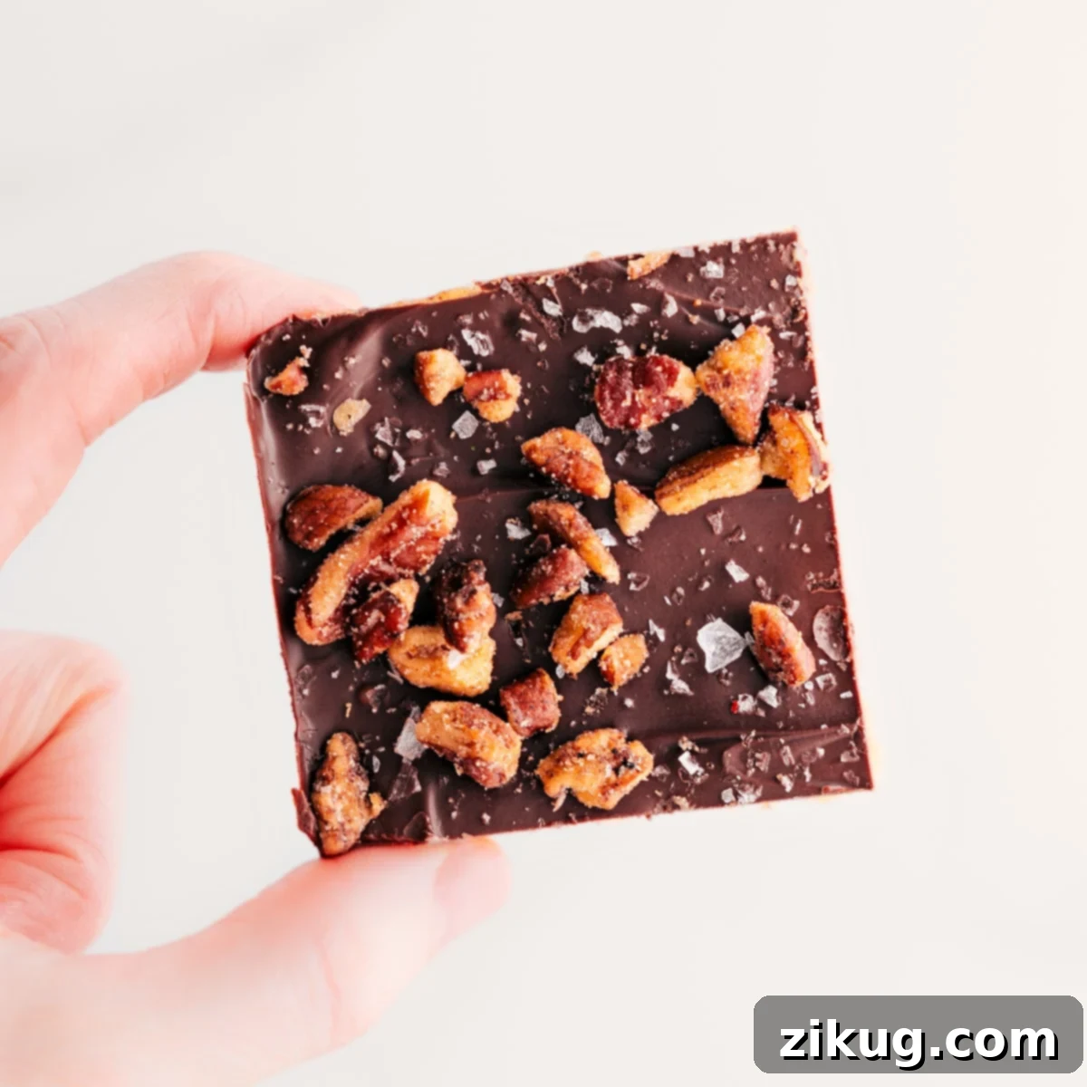 Christmas Crack Topped With Candied Pecans A Christmas Crack square is held up, topped with candied pecans. This delicious treat is perfect for the holidays.