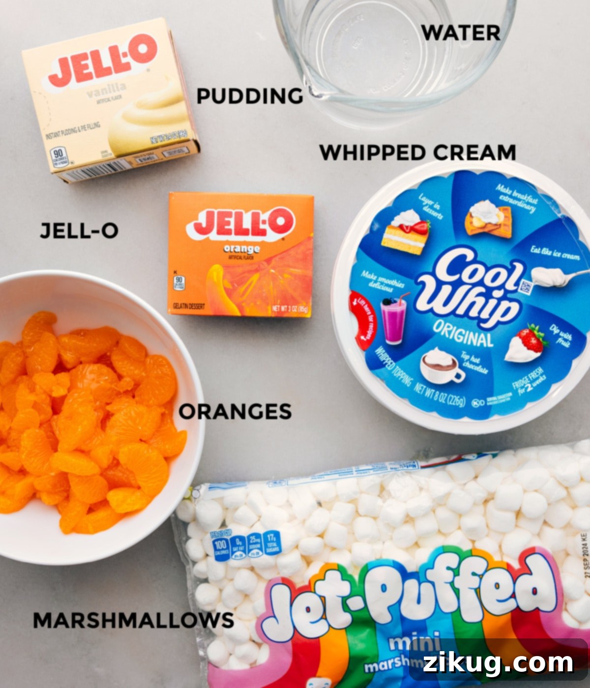 All the ingredients for this recipe including mandarins, jell-o, cool whip, and mini marshmallows prepped out for easy assembly on a kitchen counter.
