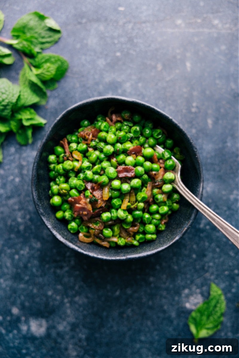 The finished gourmet Frozen Peas recipe with crisp bacon, caramelized shallots, and garlic, served warm and ready to enjoy. #easyrecipe #sidedish #delicious Overhead image of a serving bowl filled with the finished frozen peas recipe, garnished and ready to be served.