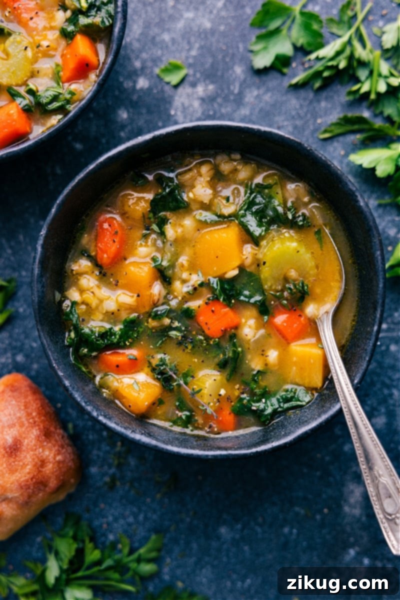 Overhead image of a steaming bowl of homemade Barley Soup, garnished with fresh parsley and a slice of crusty bread on the side.