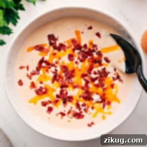 Creamy Cauliflower Soup 3 A close-up of a serving of rich and creamy cauliflower soup in a white bowl, garnished with a sprinkle of fresh herbs and a swirl of cream. The inviting texture and warm colors emphasize the comforting nature of this delicious homemade dish.