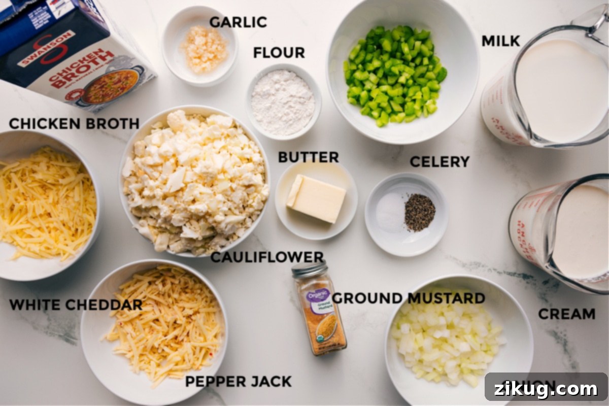 Key Ingredients For Cauliflower Soup All the essential ingredients for this creamy cauliflower soup recipe, meticulously prepped and laid out for effortless assembly. The display includes fresh cauliflower florets, blocks of sharp white cheddar and pepper jack cheese ready for shredding, rich chicken broth, creamy whole milk and heavy cream, aromatic garlic and onion, flour for thickening, butter, and a selection of seasonings like salt and pepper.