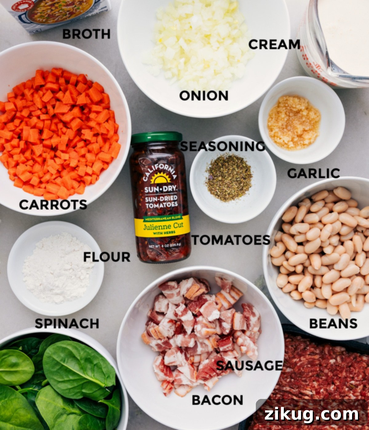 Essential Ingredients for Your Tuscan Soup Recipe A collection of fresh ingredients laid out on a table, including onions, carrots, garlic, spinach, a package of Italian sausage, bacon, sun-dried tomatoes, canned beans, broth, heavy cream, and various seasonings, ready for making Tuscan soup.