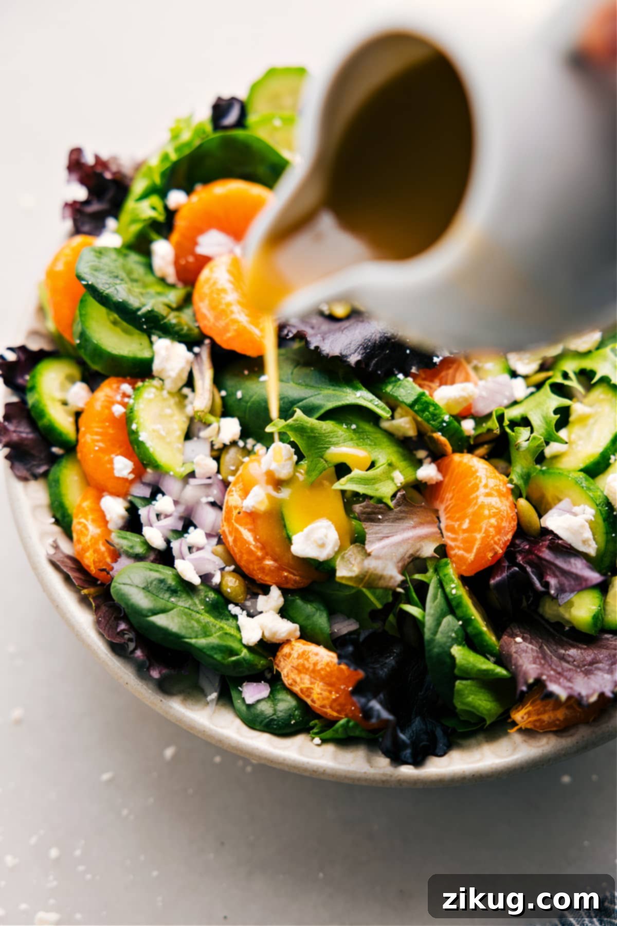 Drizzling freshly prepared White Balsamic Vinaigrette generously over a crisp, green salad, highlighting its clear and vibrant appearance.
