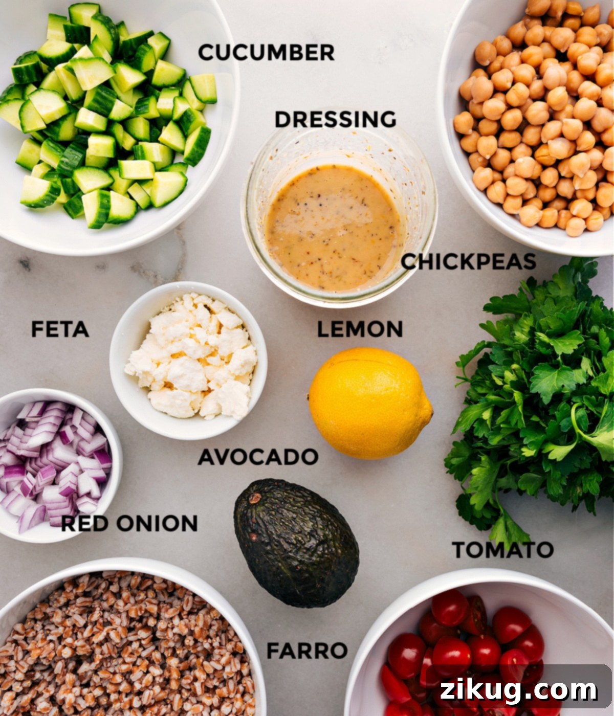 Prepped ingredients for a healthy grain bowl: homemade dressing in a jar, rinsed chickpeas, sliced cucumbers, halved cherry tomatoes, crumbled feta, a fresh lemon, cooked farro, and fresh parsley, all ready for easy assembly.
