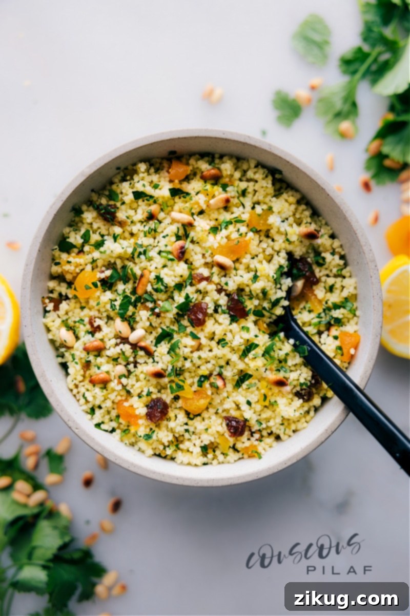 Fluffy couscous served in an elegant bowl, garnished with a vibrant mix of fresh herbs, golden dried apricots, and toasted pine nuts, showcasing its versatility and appeal as a quick, flavorful side dish.