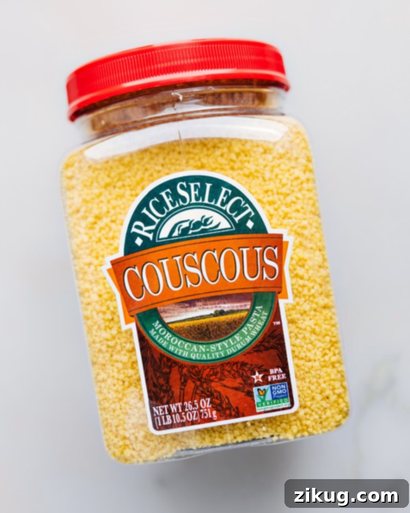 A selection of high-quality ingredients laid out for making couscous, including fine semolina grains, a bottle of rich chicken stock, fresh olive oil, and a pinch of sea salt, ready for preparation.
