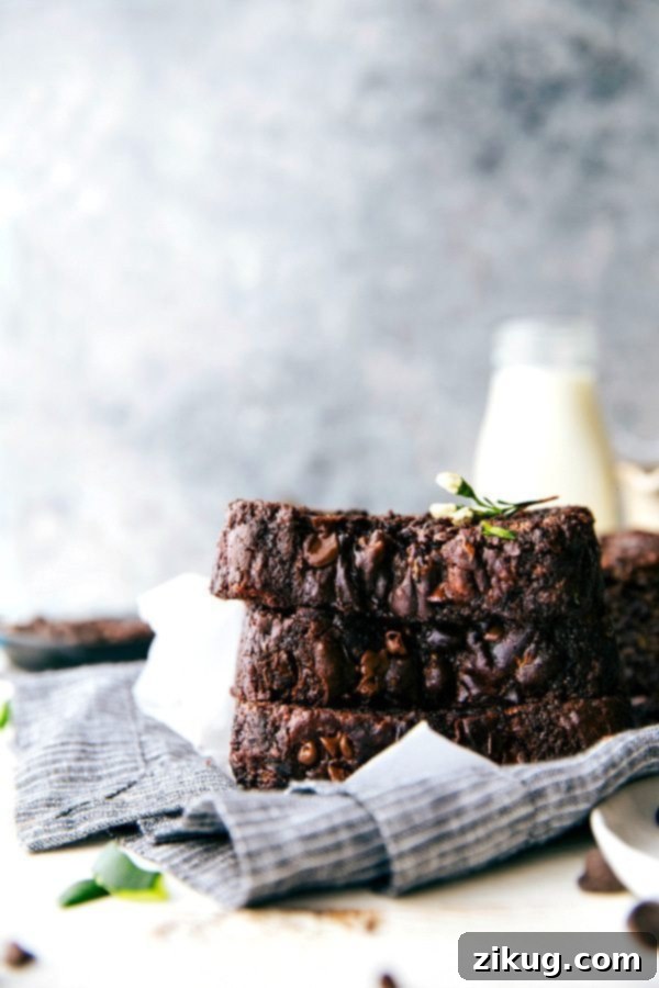 This rich Chocolate Zucchini Bread is moist, deeply chocolatey, and completely irresistible! This zucchini bread also uses better-for-you ingredients — less sugar than most zucchini bread, Greek yogurt, dark chocolate, coconut oil, blended-up oats, and of course, grated zucchini. Recipe via chelseasmessyapron #dessert #cocoa #healthy #breakfast #milk #chocolate #zucchini #bread Stacked slices of rich Chocolate Zucchini Bread showcasing its moist texture and chocolate chips