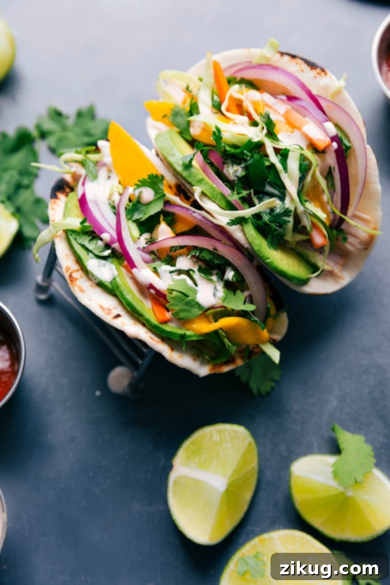 Delicious Asian Chicken Tacos: Two Tacos with Chicken, Slaw, and Sauce A close-up view of two delicious Asian chicken tacos, each generously filled with tender chicken, topped with a vibrant mango slaw, and drizzled with the signature Sriracha-lime sauce, showcasing their rich colors and inviting textures.