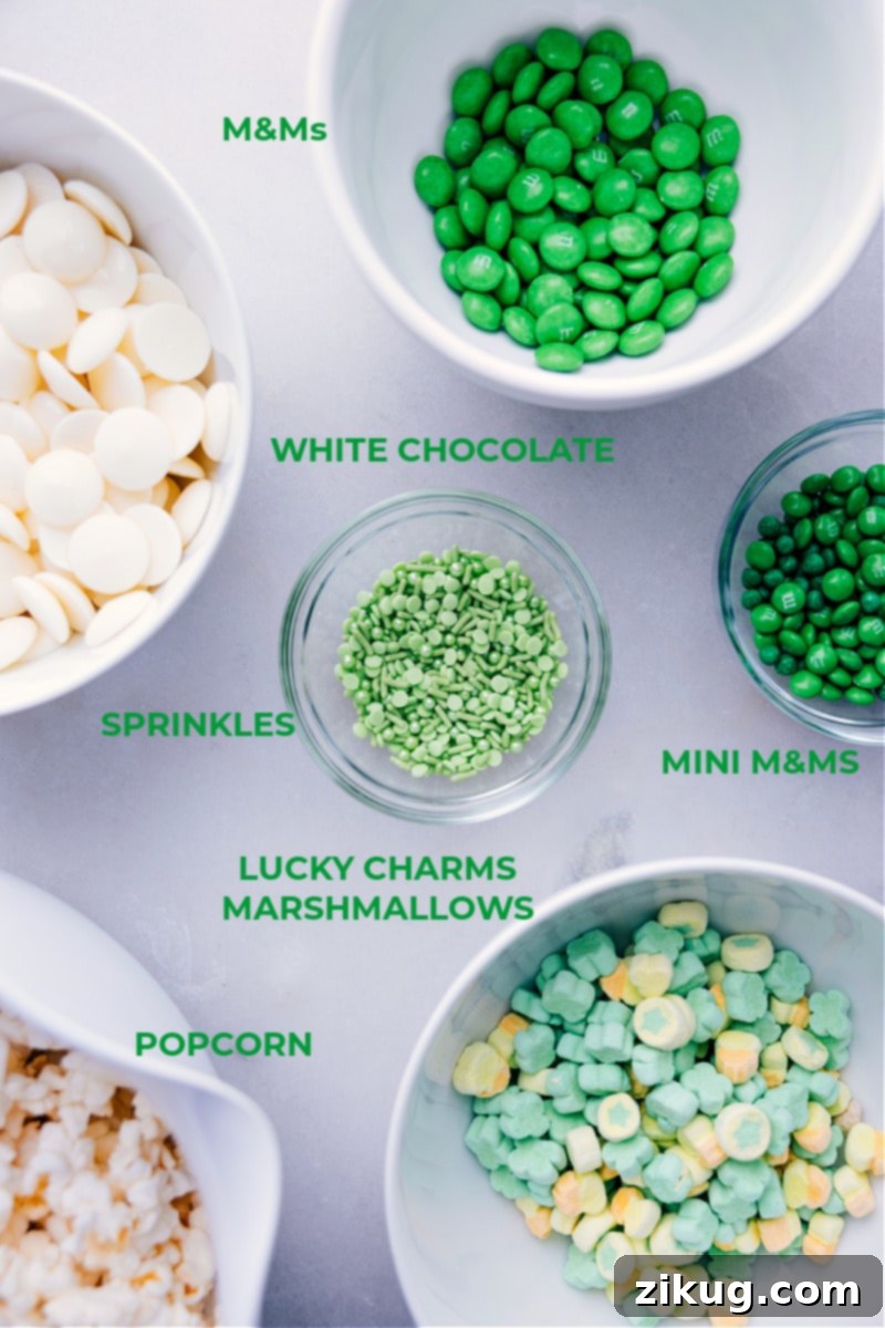 A flat lay image showcasing all the ingredients required for St. Patrick's Day Popcorn: unpopped kernels, white chocolate chips, vegetable oil, various M&M's, Lucky Charms marshmallows, and green sprinkles.