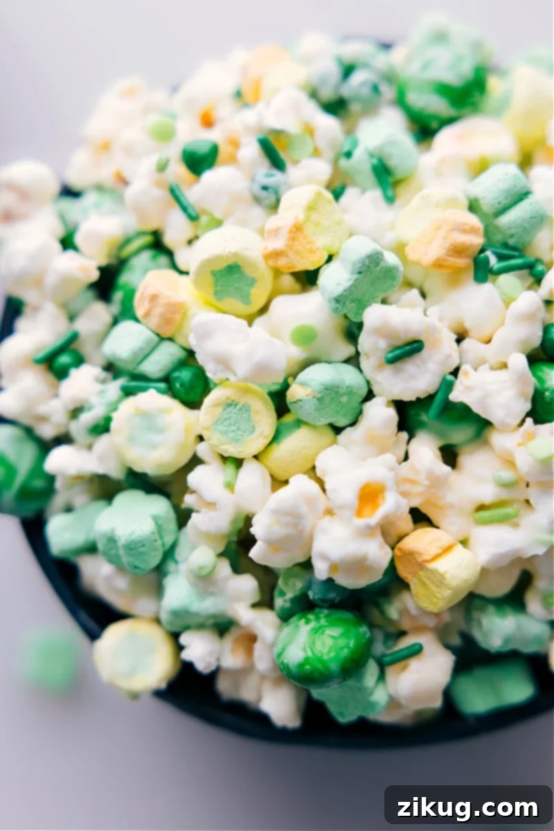 An inviting close-up, overhead shot of St. Patrick's Day Popcorn, showcasing the white chocolate coating, M&M's, Lucky Charms marshmallows, and green sprinkles, ready for enjoyment.