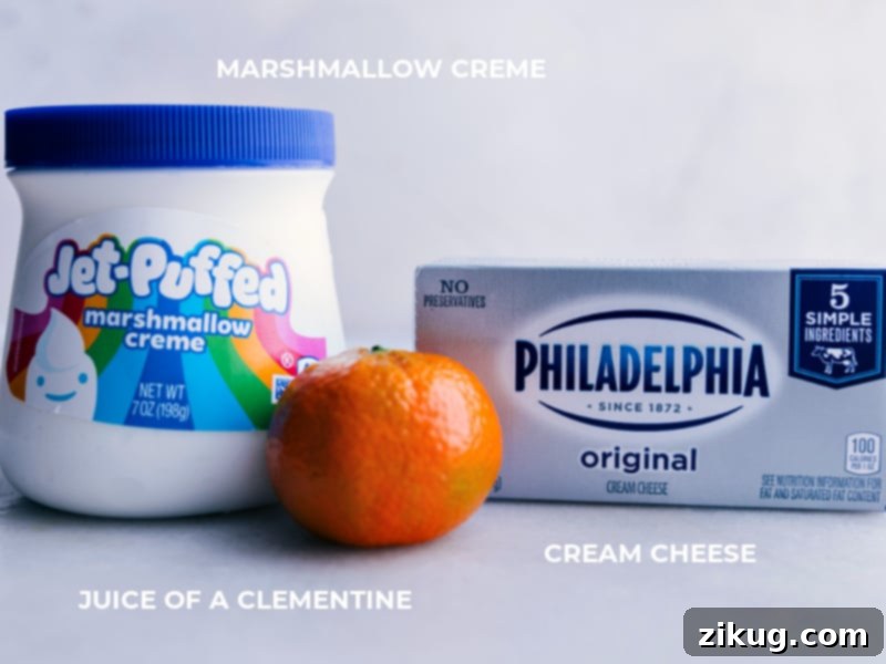 Close-up image of the three main ingredients for the fruit dip: a block of cream cheese, a tub of marshmallow creme, and a whole clementine orange
