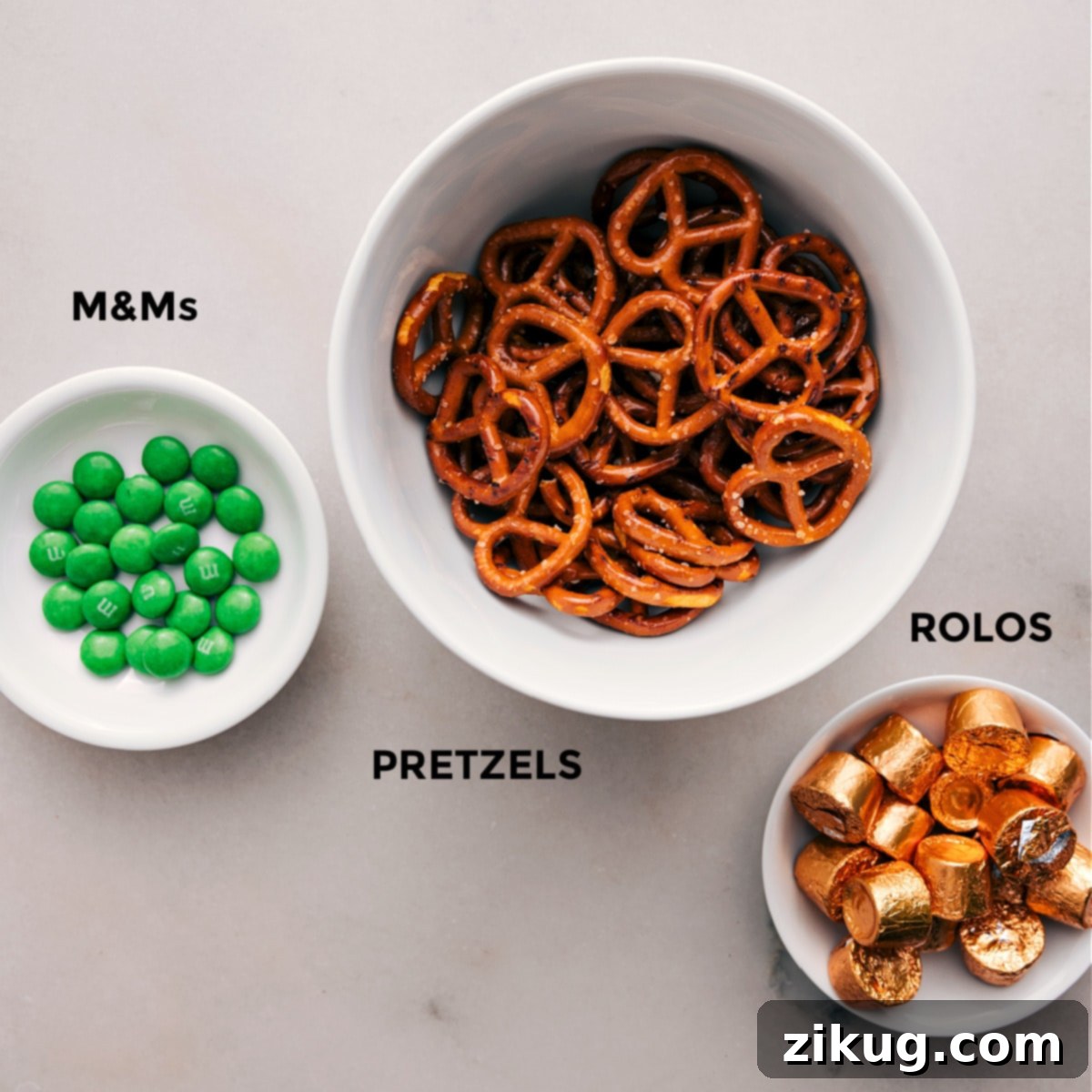 Ingredients In Leprechaun Thumbprints The 3 simple ingredients—M&Ms, pretzels, and Rolos—are prepped for easy assembly.