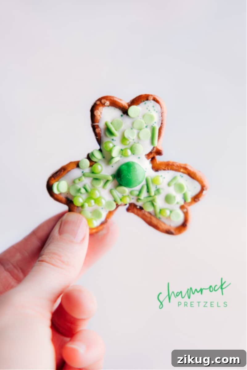 Transform a few simple ingredients into some downright delicious Pretzel Shamrocks -- perfect for St. Patrick's Day! These shamrocks double as both a sweet treat and cute table decor. Whether you're looking for a fun activity to do with the kids or a last-minute party snack, these Pretzel Shamrocks are the perfect thing to make! Hand holding up freshly made Pretzel Shamrocks with green and white chocolate.