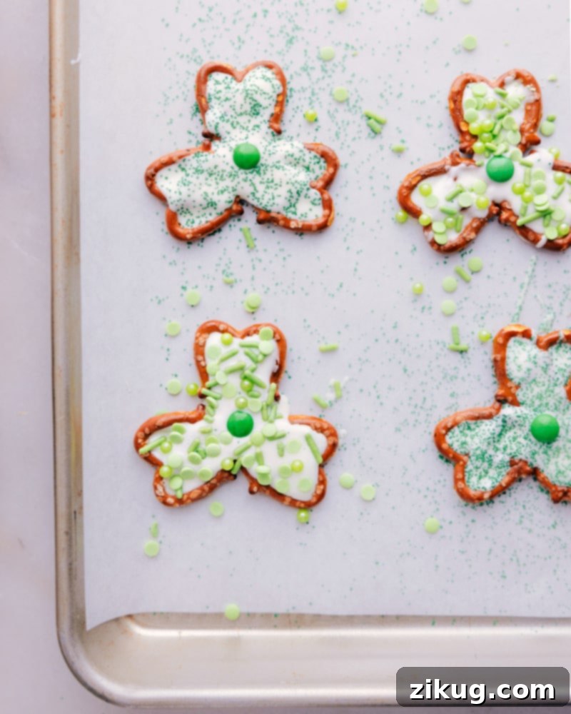 Transform a few simple ingredients into some downright delicious Pretzel Shamrocks! These shamrocks double as both a sweet treat and cute table decor. Whether you're looking for a fun activity to do with the kids or a last-minute party snack, these Pretzel Shamrocks are the perfect thing to make! Overhead shot of multiple Pretzel Shamrocks arranged on a white tray, showcasing their festive appearance.
