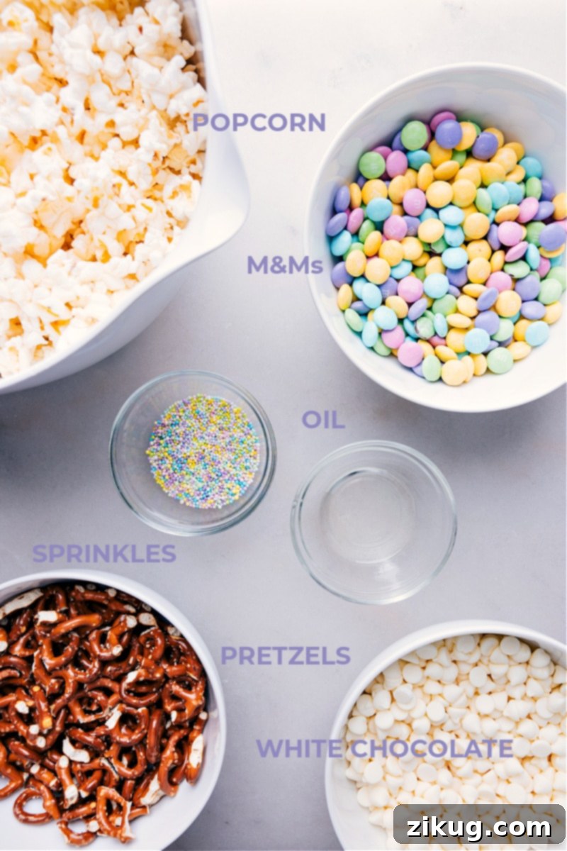 Close-up shot of all the essential ingredients laid out for making Easter Popcorn: plain popcorn, mini pretzels, pastel M&M's, white chocolate chips, and a small bowl of vegetable oil.