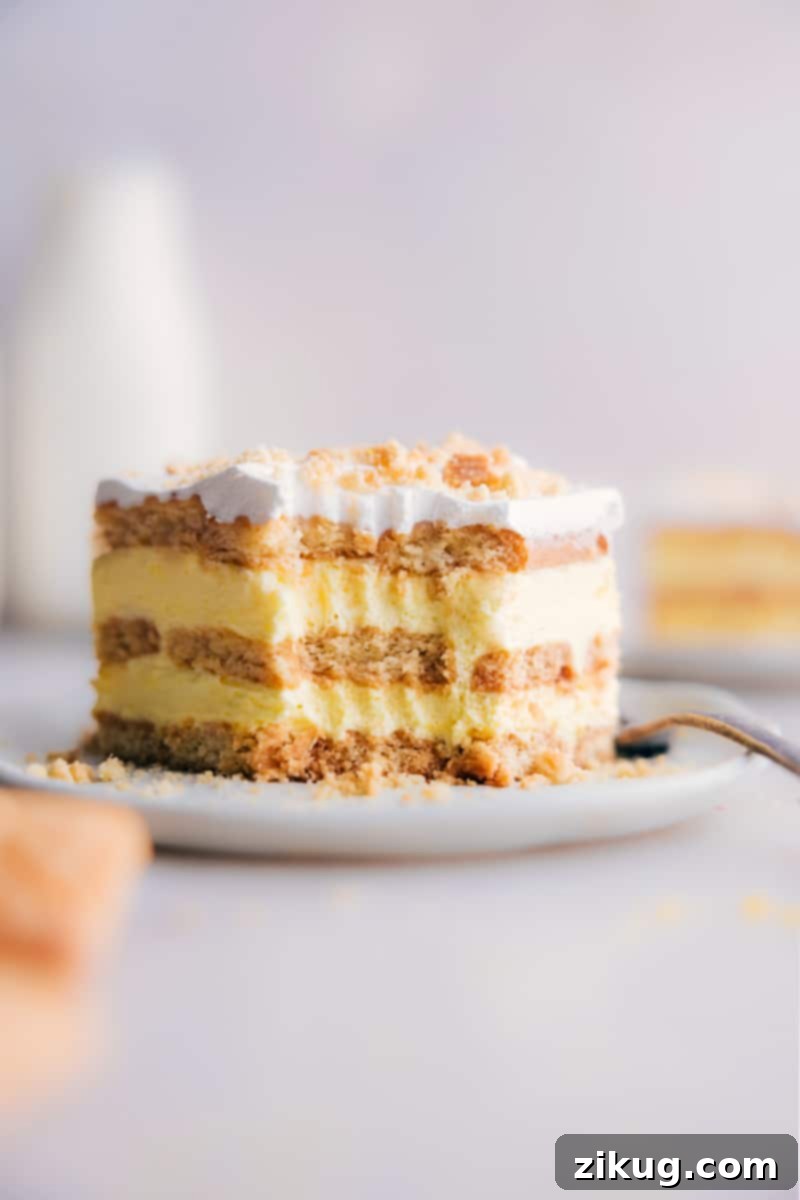 A close-up image of a slice of Lemon Icebox Cake, with a small bite taken out, highlighting the fluffy lemon filling and cookie layers.