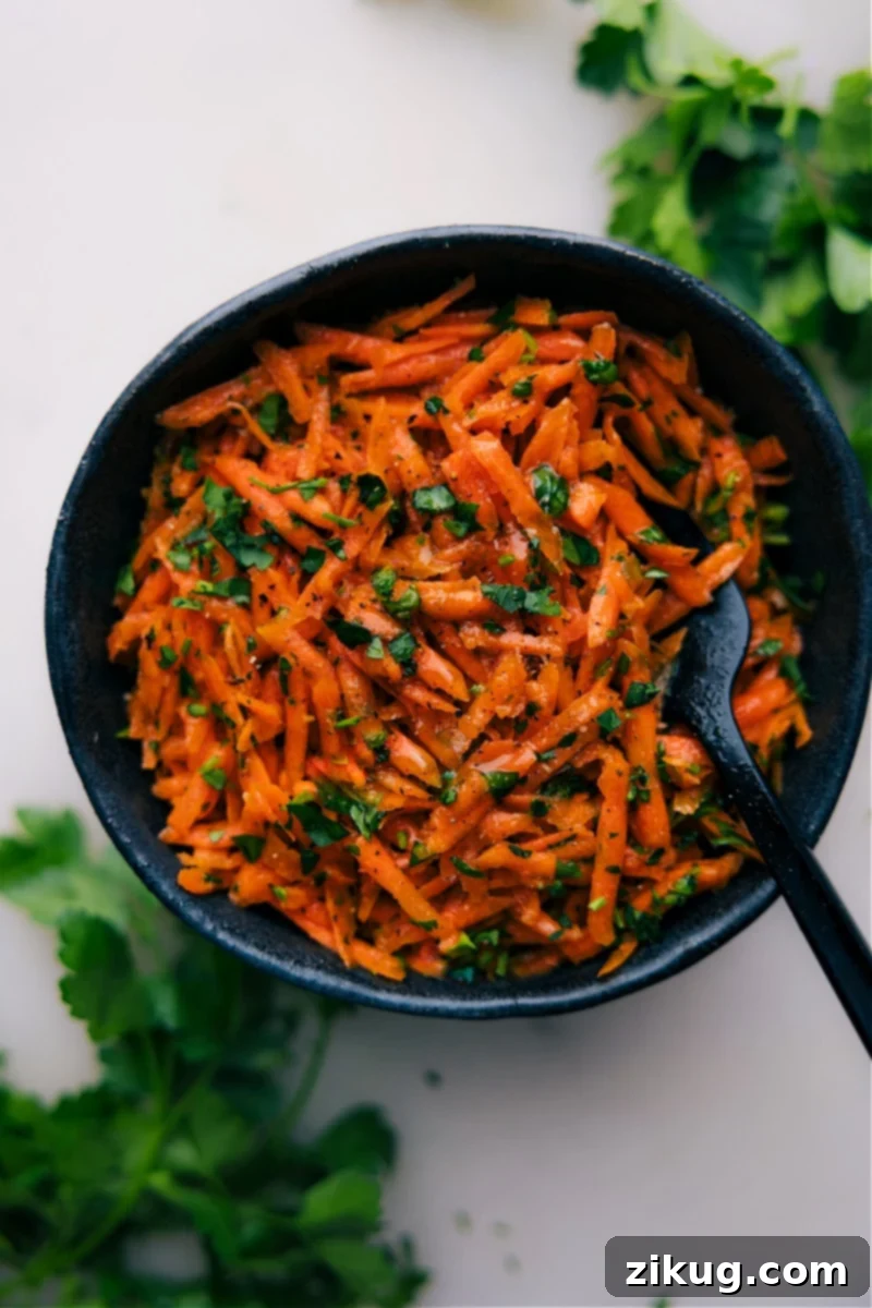 A vibrant French Carrot Salad featuring freshly grated carrots, diced shallots, and chopped parsley, dressed in a zesty lemon-honey-Dijon vinaigrette. Perfect for any meal. Overhead image of a vibrant French Carrot Salad in a white bowl, garnished with fresh parsley.