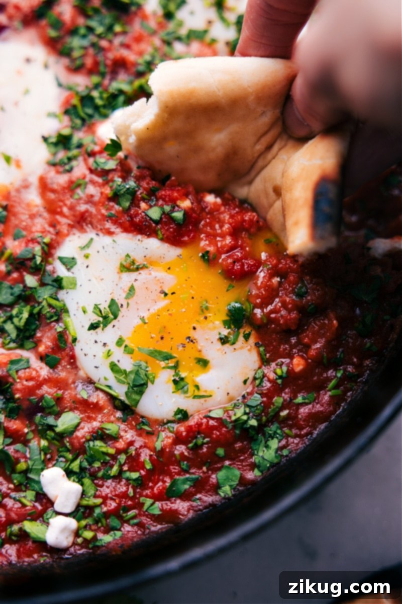 Shakshuka: A Vibrant Middle Eastern and Mediterranean Breakfast Staple Overhead image of a vibrant Shakshuka dish in a skillet, garnished with fresh herbs, ready to be served with bread.