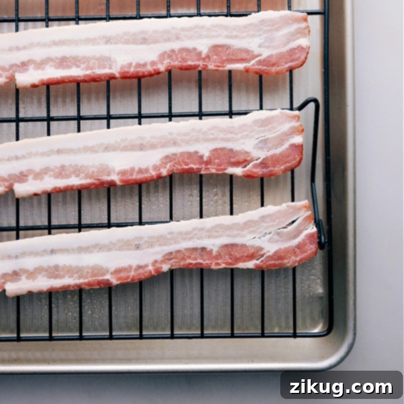 Bacon strips neatly arranged on a cooling rack over a foil-lined baking sheet, ready for the oven.