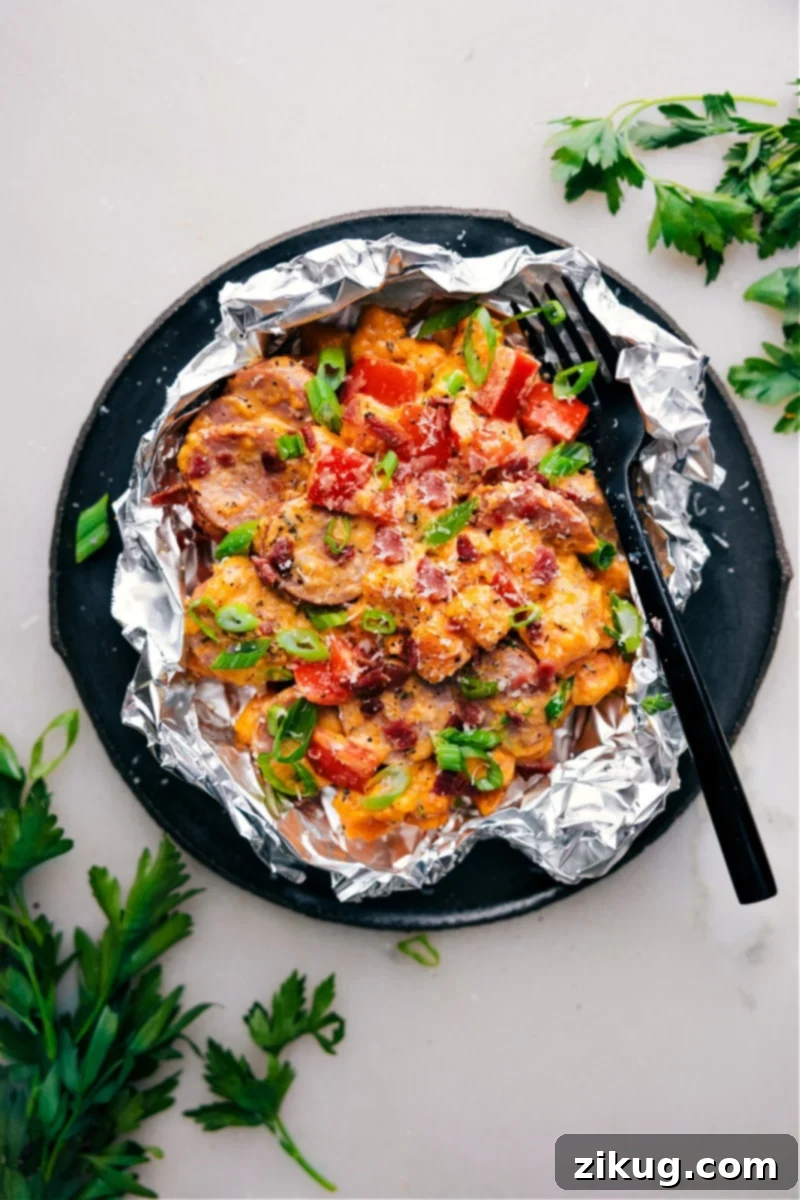 Creamy Sweet Potato and Sausage in Foil Packs: featuring tender sweet potatoes, smoky sausage, and a luscious, savory cream sauce! These foil packs are bursting with flavor and sure to become a new favorite in your household. The best part? Cleanup is a breeze! Recipe via chelseasmessyapron #dinner #quick #easy #simple #familyfriendly #kidfriendly #campingfood #campingdinner #creamy #sweetpotato #sausage #foilpack Overhead image of the Creamy Sweet Potato and Sausage in a foil packet, showcasing tender sweet potatoes, smoky sausage, and a luscious cream sauce.