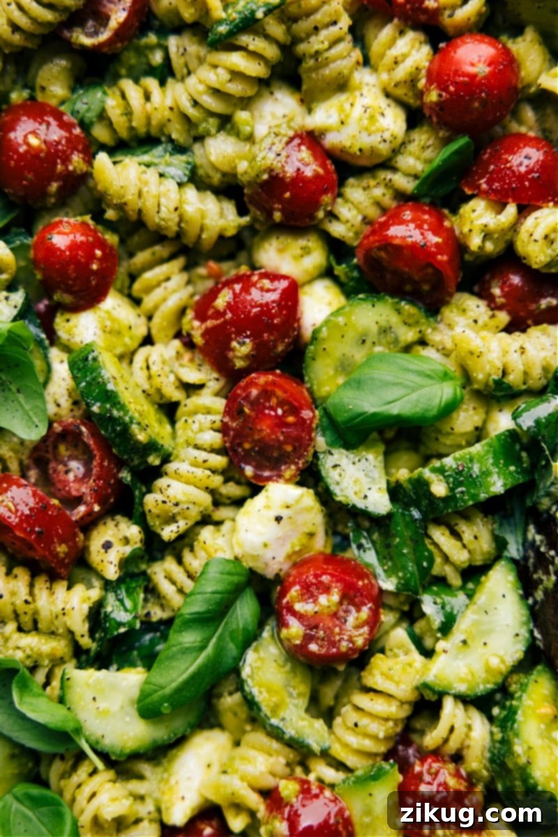 Pesto Pasta Salad combines rotini pasta, juicy cherry tomatoes, crisp cucumbers, and creamy mozzarella pearls, all tossed in a luscious, herbaceous basil pesto dressing. The creamy dressing is what takes this salad to the next level, with its tangy notes of mayo, sour cream, and dijon mustard, perfectly balanced by the bright, zesty flavor of fresh basil-pesto and lemon juice. This salad is easy to make and sure to be a hit wherever it's served! Recipe via chelseasmessyapron #dinner #quick #easy #simple #familyfriendly #kidfriendly #sidedish #noodles #bbq #pesto #pastasalad An up-close overhead image of a bowl of Pesto Pasta Salad, perfectly garnished and presented as an ideal side dish.